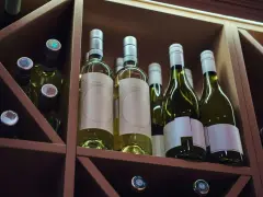 Butelki białego wina w drewnianym regale. Zastanawiasz się, ile może stać otwarte wino? Te butelki czekają na degustację.