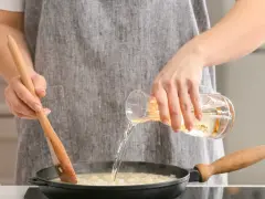 Gotowanie z płynem, który może zawierać alkohol. Czy alkohol wyparowuje podczas gotowania? Ktoś miesza potrawę drewnianą łyżką i dolewa płyn z kieliszka.