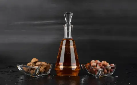 Amaretto co to? Bursztynowy likier w karafce, obok miseczki z migdałami i orzechami laskowymi.