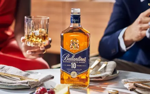 Elegancka kolacja z whisky i piwem w tle. Butelka Ballantine's 10 Years Old na stole, obok kieliszek z bursztynowym trunkiem.