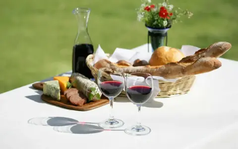 Dwa kieliszki pełne rubinowego pinot noir wina, obok deska serów, wędlin i kosz świeżego pieczywa.