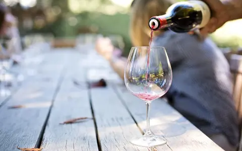Czerwone wino nalewane do kieliszka na drewnianym stole. Idealny moment, by dowiedzieć się, jak degustować wino.