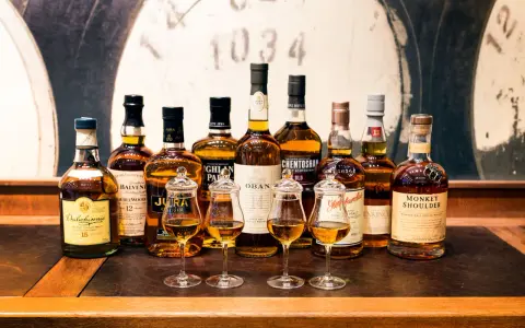 Wybór między single malt czy blended: rząd butelek szkockiej whisky, cztery kieliszki z bursztynowym płynem.