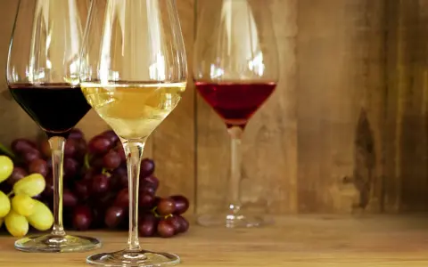 Trzy kieliszki z winem: czerwonym, białym i różowym, obok kiście winogron. Idealne na prosty przepis na wino.