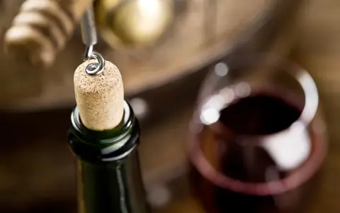 Korek wyciągany z butelki wina, kieliszek czerwonego wina i beczka. Czy wino ma datę ważności? To pytanie zadaje sobie wielu miłośników tego trunku.