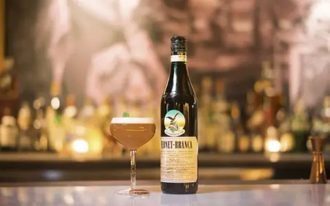 Fernet Stock z czym pić? Oto propozycja drinka z butelką Fernet-Branca i kieliszkiem koktajlu na barze.