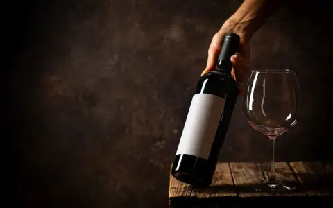 Dłoń trzyma butelkę wina, obok stoi pusty kieliszek. Zastanawiasz się, ile może stać zamknięte wino?