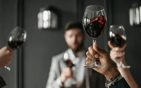 Wzniesione kieliszki z czerwonym winem, w tle mężczyzna w garniturze. Ciesz się chwilą z dobrym winem w kieliszku.