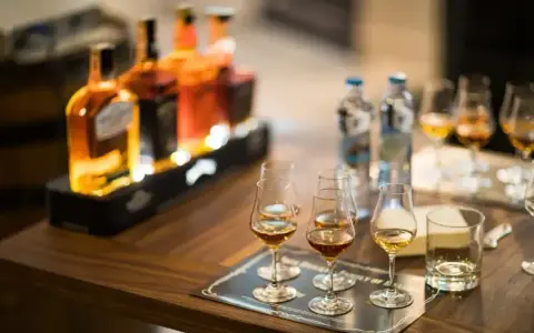 Degustacja whisky, czy to bimber? Butelki i kieliszki z bursztynowym trunkiem na drewnianym stole.