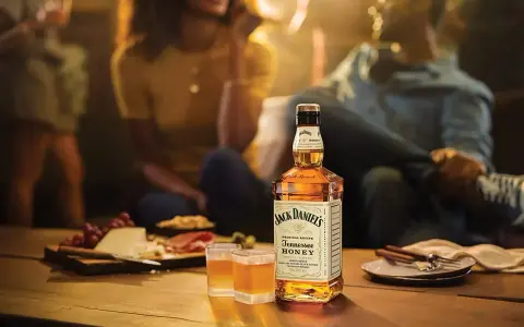 Jack Daniel's Honey z czym pić? Idealnie smakuje solo, z lodem lub jako dodatek do drinków. Na stole ser, winogrona i przekąski.