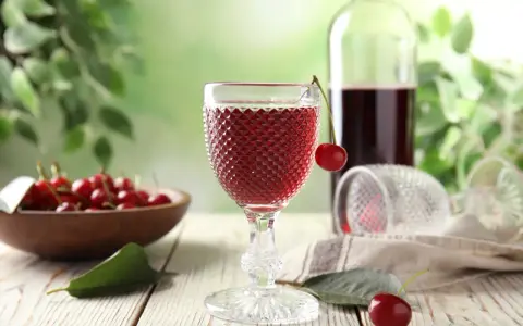 Wytrawne wino z owocami wiśni, podane w ozdobnym kieliszku, z miseczką pełną świeżych wiśni w tle.