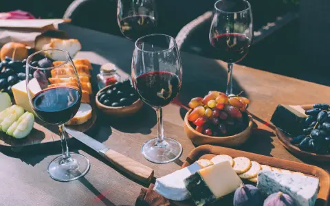 Degustacja merlot: jakie to wino? Kieliszki pełne czerwonego wina, deska serów, winogrona, oliwki i pieczywo tworzą idealną kompozycję.