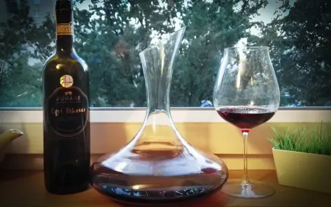 Butelka wina Egri Bikavér, karafka i kieliszek z czerwonym winem. Czas na degustację wina bycza krew.