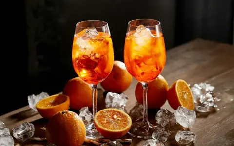 Dwa kieliszki orzeźwiającego aperol z colą, ozdobione pomarańczami i lodem, kuszą letnim smakiem.