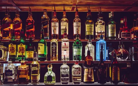 Różnorodne podstawowe alkohole do drinków: whisky, gin, tequila, likiery, stoją na półkach baru, gotowe do przygotowania koktajli.
