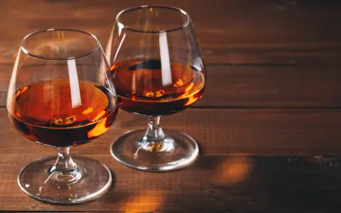 Dwa kieliszki z bursztynowym płynem, być może amerykańska whisky z kukurydzy, stoją na drewnianym stole.