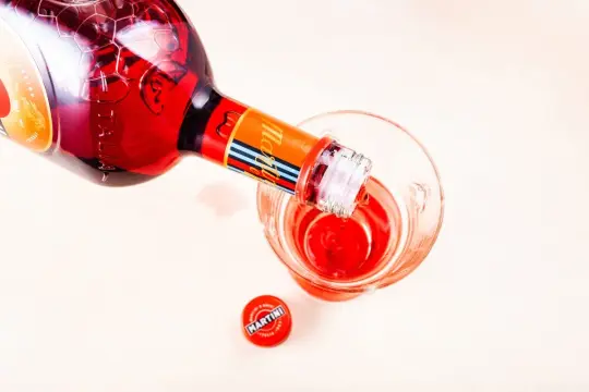 Nalewanie czerwonego Martini Fiero drinka do szklanki. Obok leży czerwona zakrętka z logo Martini.