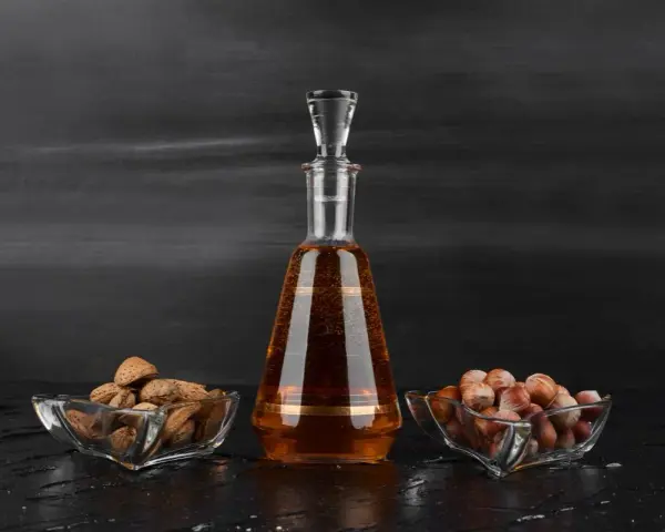 Amaretto co to? Bursztynowy likier w karafce, obok miseczki z migdałami i orzechami laskowymi.