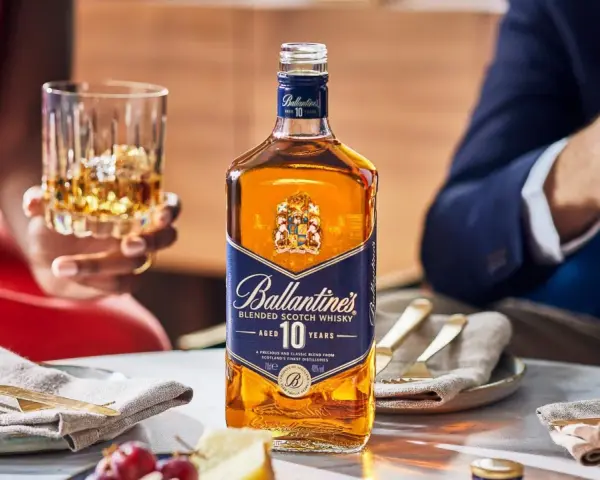Elegancka kolacja z whisky i piwem w tle. Butelka Ballantine's 10 Years Old na stole, obok kieliszek z bursztynowym trunkiem.