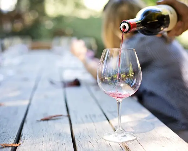 Czerwone wino nalewane do kieliszka na drewnianym stole. Idealny moment, by dowiedzieć się, jak degustować wino.