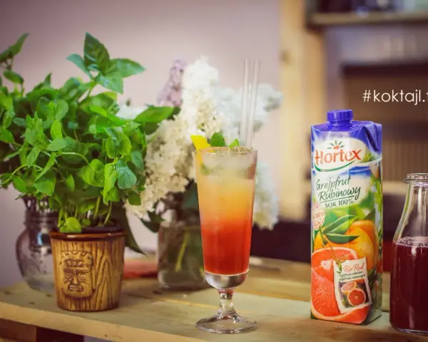 Kolorowy drink z lodem i słomkami, obok sok grejpfrutowy Hortex i butelka z ciemnym płynem.