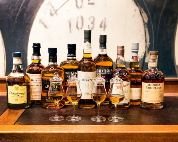 Wybór między single malt czy blended: rząd butelek szkockiej whisky, cztery kieliszki z bursztynowym płynem.