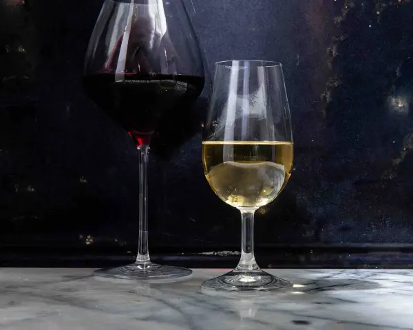 Dwa kieliszki z winem: czerwonym i białym. Białe wino, w tym wino extra dry, lśni w świetle.