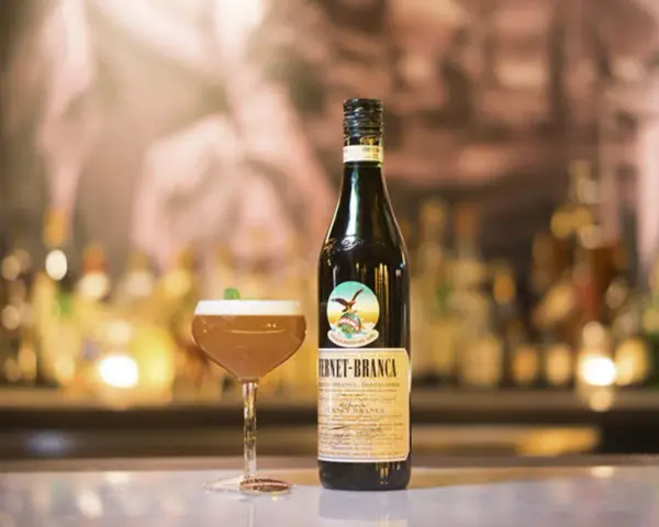 Fernet Stock z czym pić? Oto propozycja drinka z butelką Fernet-Branca i kieliszkiem koktajlu na barze.