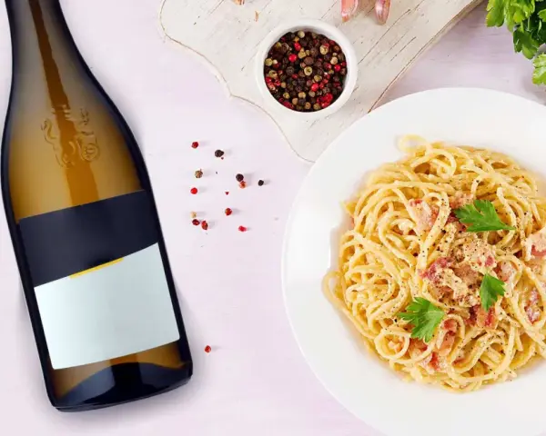 Idealne jakie wino do carbonary? Obok talerza z pysznym makaronem i butelki białego wina, pieprz i natka pietruszki.