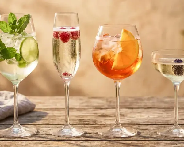 Cztery drinki na drewnianym stole: mojito, prosecco z malinami, Aperol Spritz i kieliszek prosecco z jeżyną. Idealne inspiracje, jak pić prosecco i inne orzeźwiające napoje.