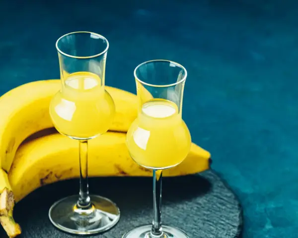 Dwa kieliszki z żółtym likierem bananowym, obok pęk bananów. Idealny na domowy likier bananowy przepis.