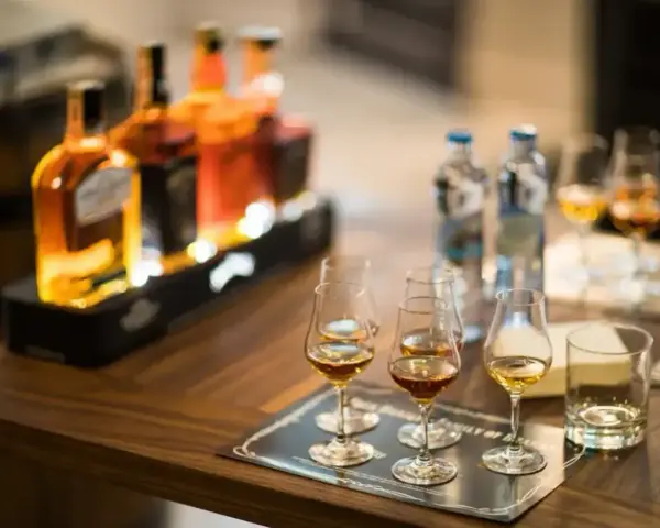 Degustacja whisky, czy to bimber? Butelki i kieliszki z bursztynowym trunkiem na drewnianym stole.