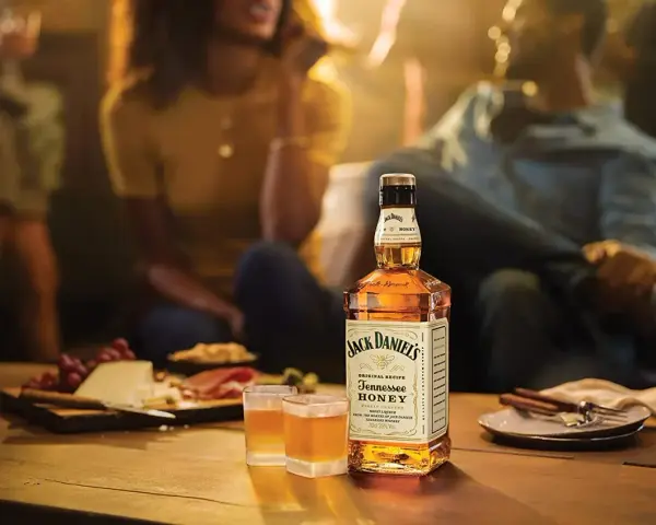 Jack Daniel's Honey z czym pić? Idealnie smakuje solo, z lodem lub jako dodatek do drinków. Na stole ser, winogrona i przekąski.
