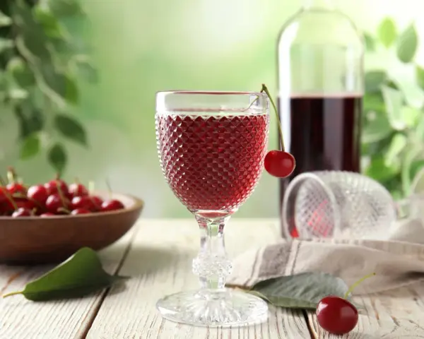 Wytrawne wino z owocami wiśni, podane w ozdobnym kieliszku, z miseczką pełną świeżych wiśni w tle.
