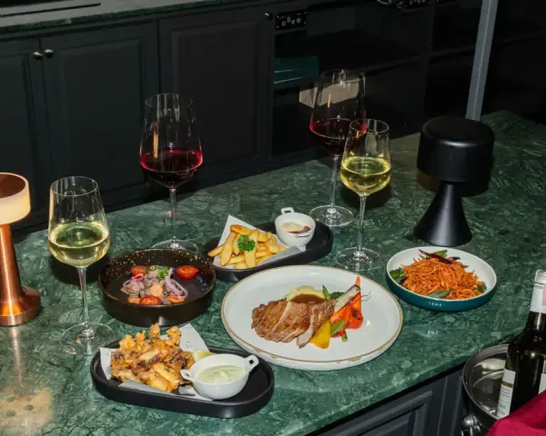 Elegancka kolacja z daniami i winem. Czy to chardonnay, jakie to wino? Obok kieliszki z białym i czerwonym winem, mięso, frytki i sałatka.