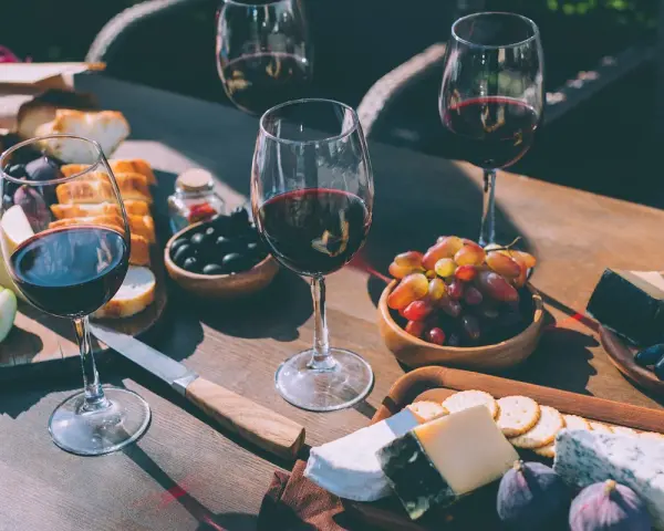 Degustacja merlot: jakie to wino? Kieliszki pełne czerwonego wina, deska serów, winogrona, oliwki i pieczywo tworzą idealną kompozycję.