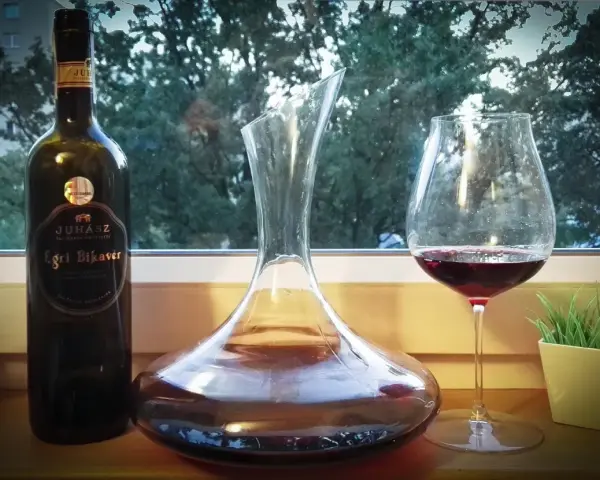 Butelka wina Egri Bikavér, karafka i kieliszek z czerwonym winem. Czas na degustację wina bycza krew.