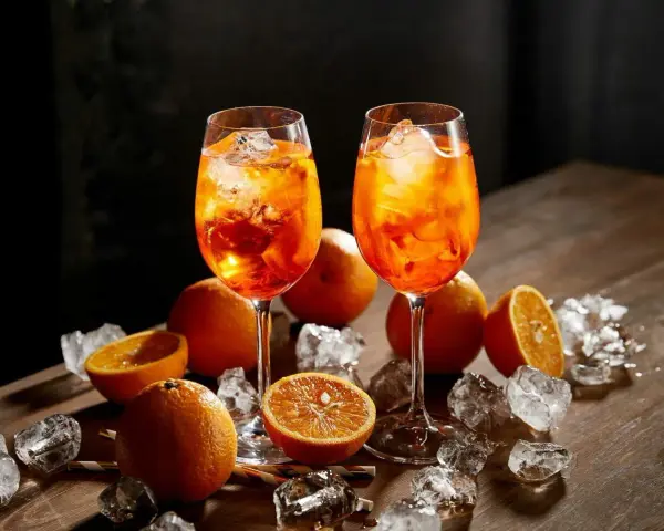 Dwa kieliszki orzeźwiającego aperol z colą, ozdobione pomarańczami i lodem, kuszą letnim smakiem.