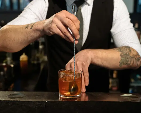 Barman miesza kostki lodu z bursztynowym płynem w szklance. Idealny **whisky z tonikiem** gotowy do podania.