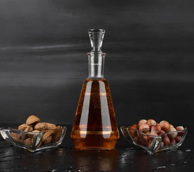 Amaretto co to? Bursztynowy likier w karafce, obok miseczki z migdałami i orzechami laskowymi.