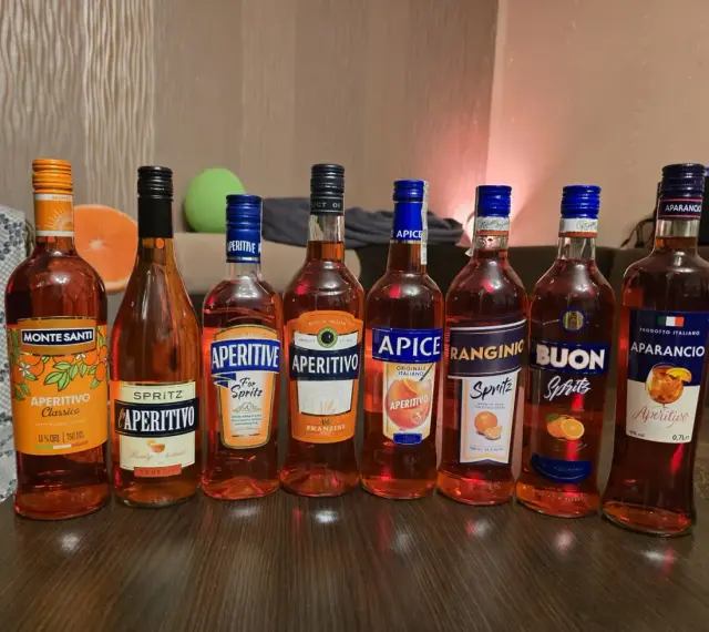 Rząd butelek aperitifów: Monte Santi, L'Aperitivo, Aperitive, Aperitivo Franzini, Apice, Ranginio, Buon, Aparancio. Idealne na drinki, jak Campari czy Aperol.