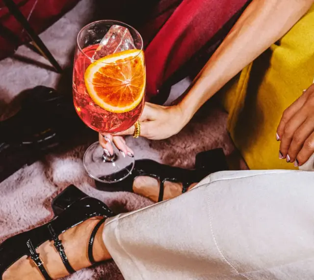 Elegancki drink z pomarańczą i lodem. Czy to wermut? Stylowe buty i złota biżuteria dopełniają scenę.
