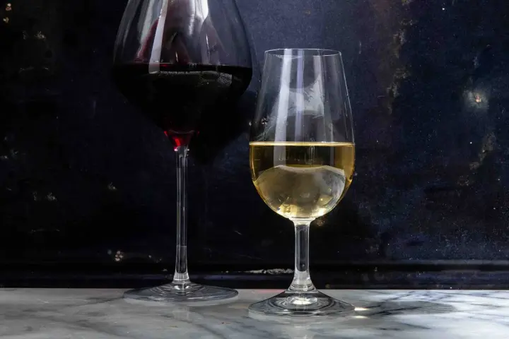 Dwa kieliszki z winem: czerwonym i białym. Białe wino, w tym wino extra dry, lśni w świetle.