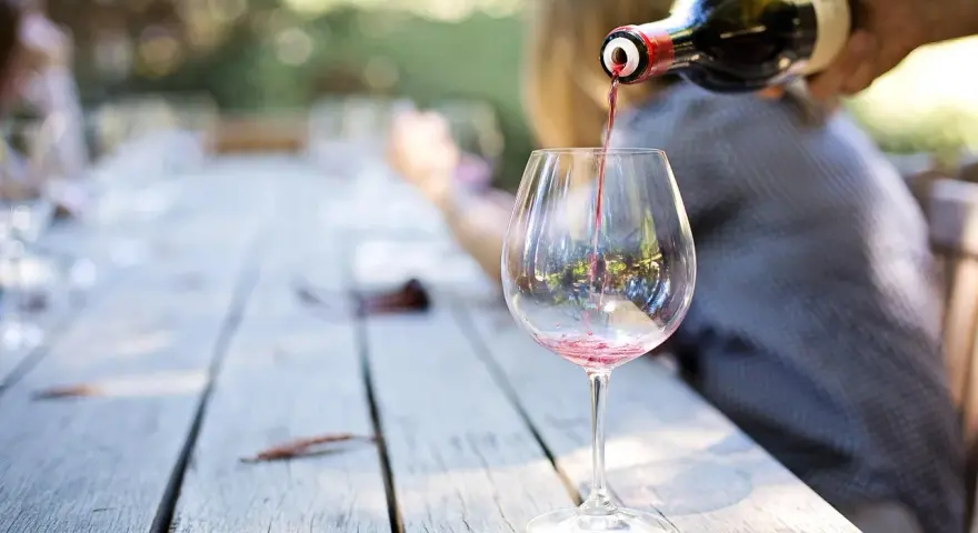 Czerwone wino nalewane do kieliszka na drewnianym stole. Idealny moment, by dowiedzieć się, jak degustować wino.