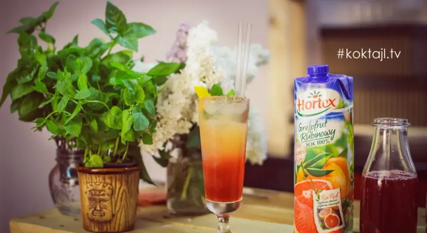 Kolorowy drink z lodem i słomkami, obok sok grejpfrutowy Hortex i butelka z ciemnym płynem.