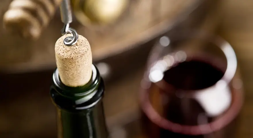 Korek wyciągany z butelki wina, kieliszek czerwonego wina i beczka. Czy wino ma datę ważności? To pytanie zadaje sobie wielu miłośników tego trunku.
