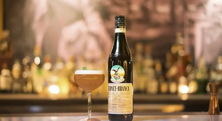 Fernet Stock z czym pić? Oto propozycja drinka z butelką Fernet-Branca i kieliszkiem koktajlu na barze.