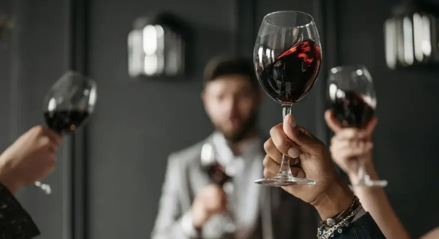 Wzniesione kieliszki z czerwonym winem, w tle mężczyzna w garniturze. Ciesz się chwilą z dobrym winem w kieliszku.