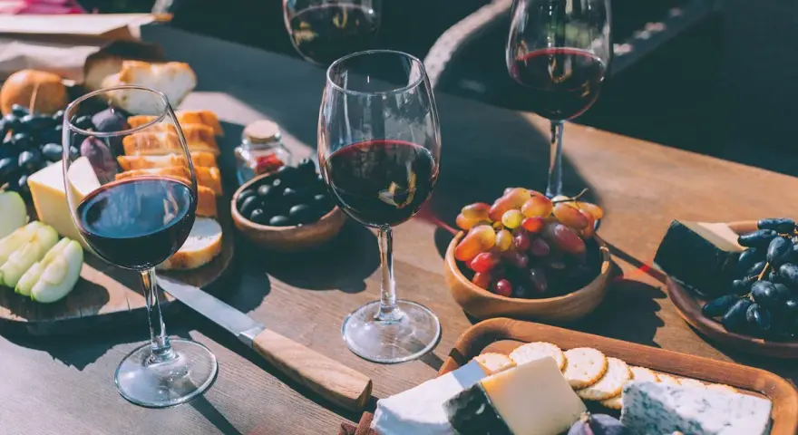 Degustacja merlot: jakie to wino? Kieliszki pełne czerwonego wina, deska serów, winogrona, oliwki i pieczywo tworzą idealną kompozycję.