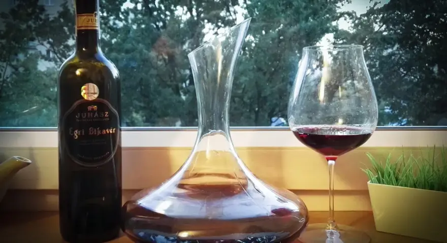 Butelka wina Egri Bikavér, karafka i kieliszek z czerwonym winem. Czas na degustację wina bycza krew.